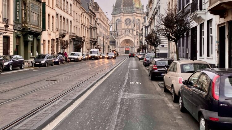 Stadtstraße mit Fahrradspur, parkenden Autos und Blick auf die Église Sainte-Marie in Brüssel.